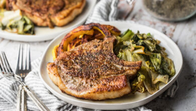 Chinese five spice pork chops with sauteed escarole and roasted delicata squash on white plates, white napkin, two forks.