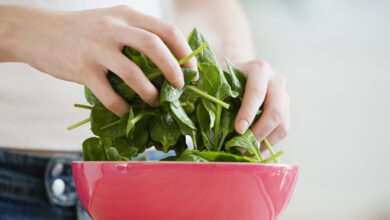 Hands tossing fresh spinach in a red bowl.