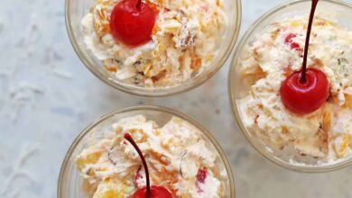 creamy ambrosia fruit salad in three small cups with a cherry on top