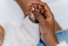 A person holds the hand of a baby in this stock image (Pexels/William Fortunato)